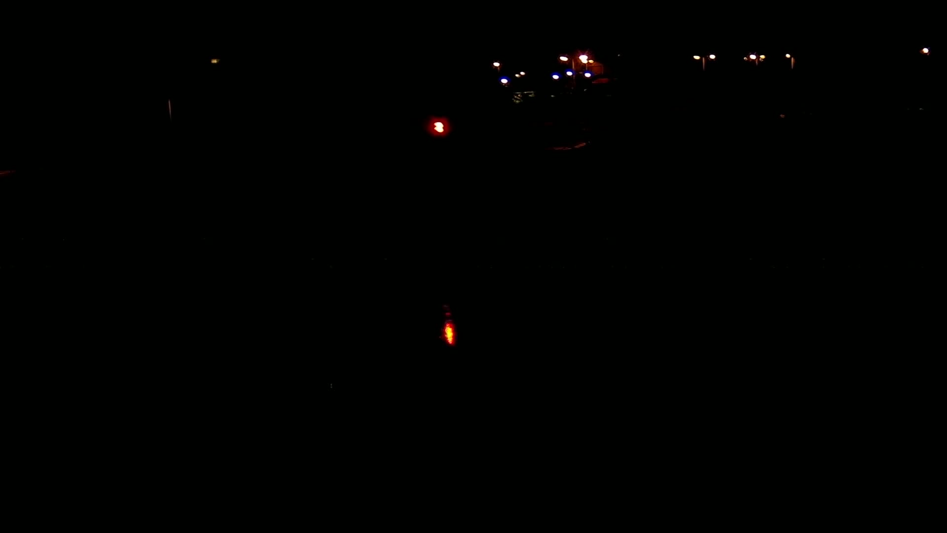 A nighttime scene shows a few distant lights and a single, closer red light in an otherwise dark environment.