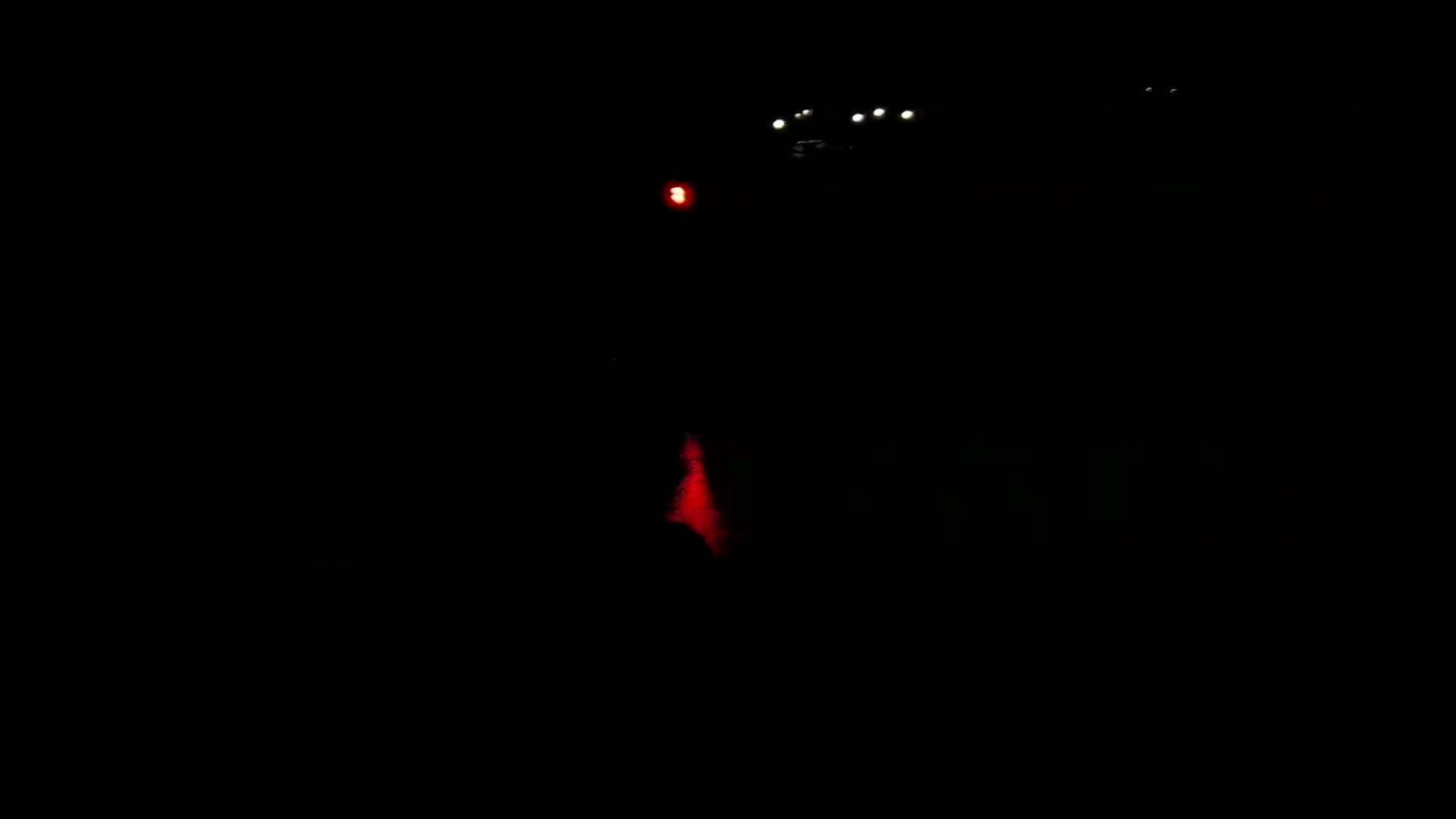 A dark scene at night shows a faint red light and several distant white lights.