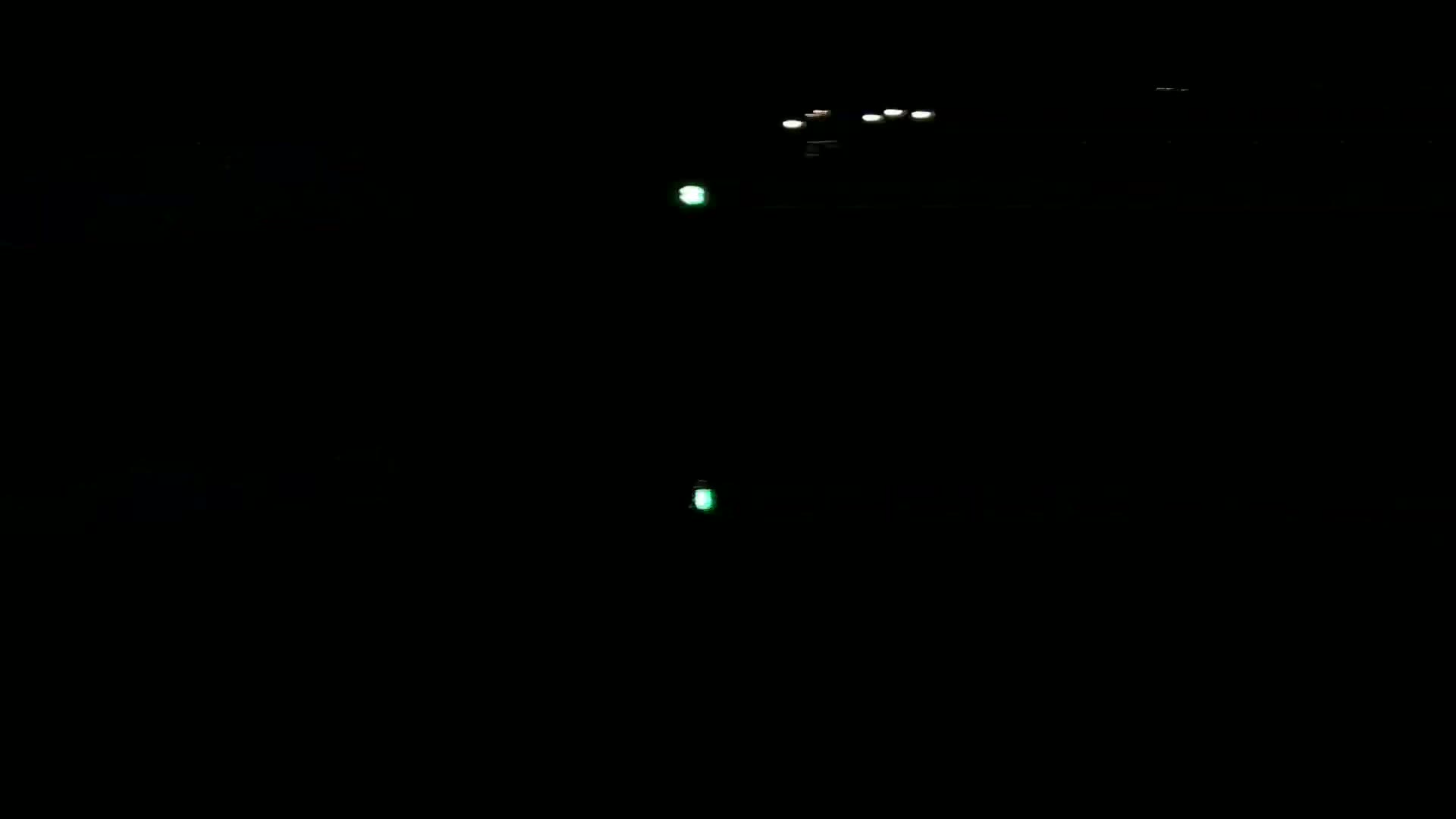 Faint lights from vehicles and two small green lights are visible in the inky blackness of night.