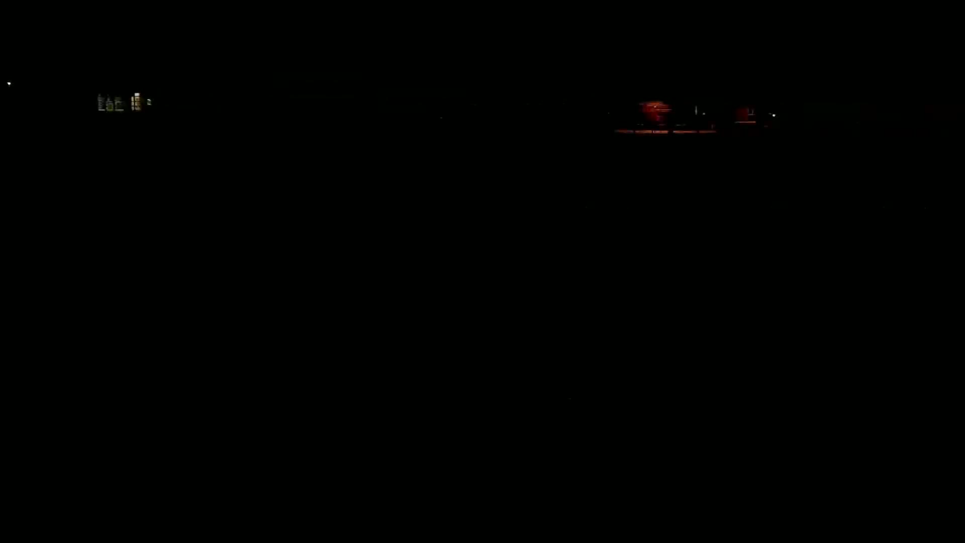 A dimly lit, nighttime scene shows a few illuminated buildings in the distance.