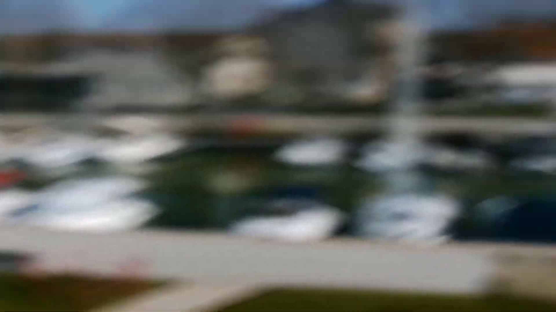 A blurry image shows many boats moored in a marina on a partly cloudy day.