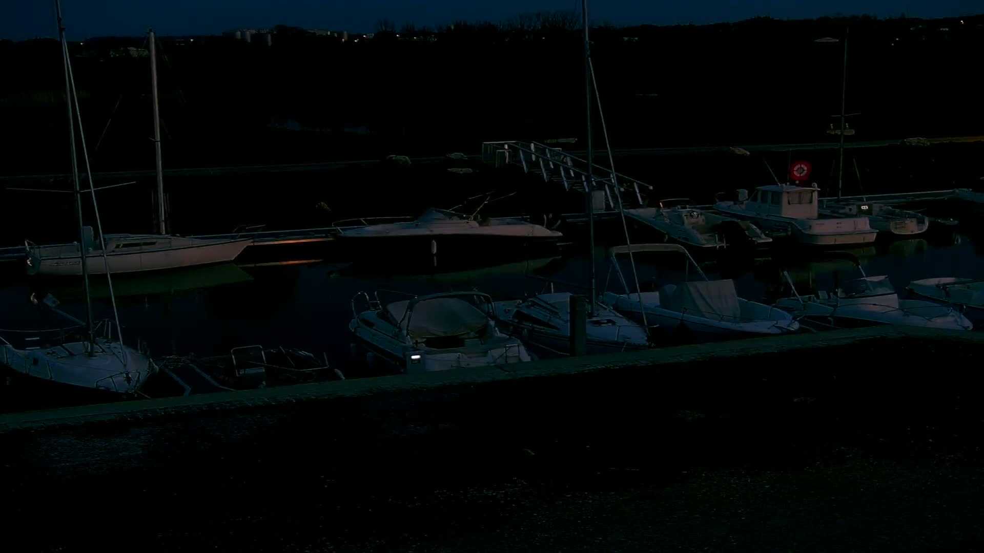 Several boats and sailboats are moored at a dock at night under a dark sky.