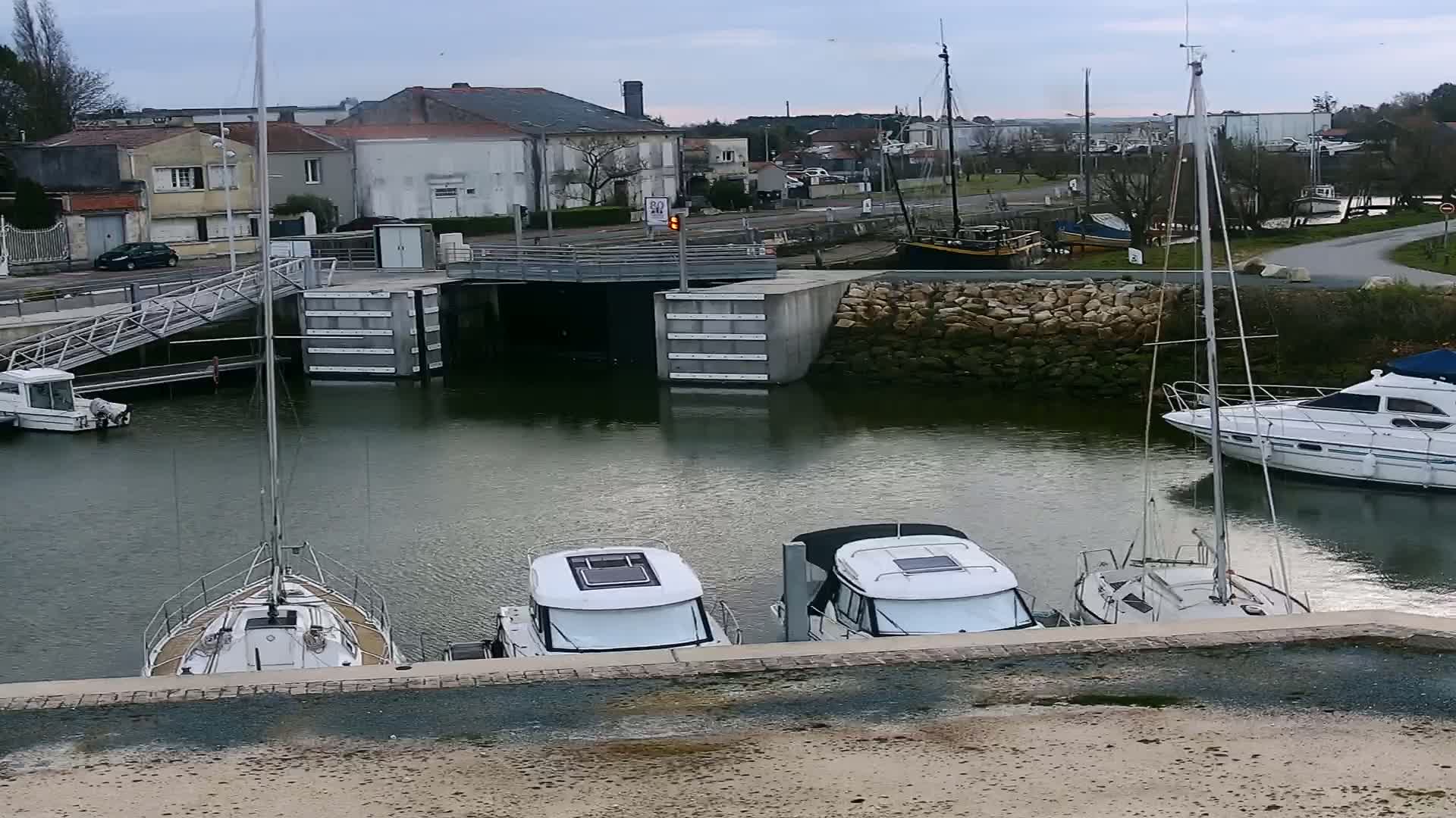 Several boats are moored in a calm harbor next to a stone wall under a cloudy sky.