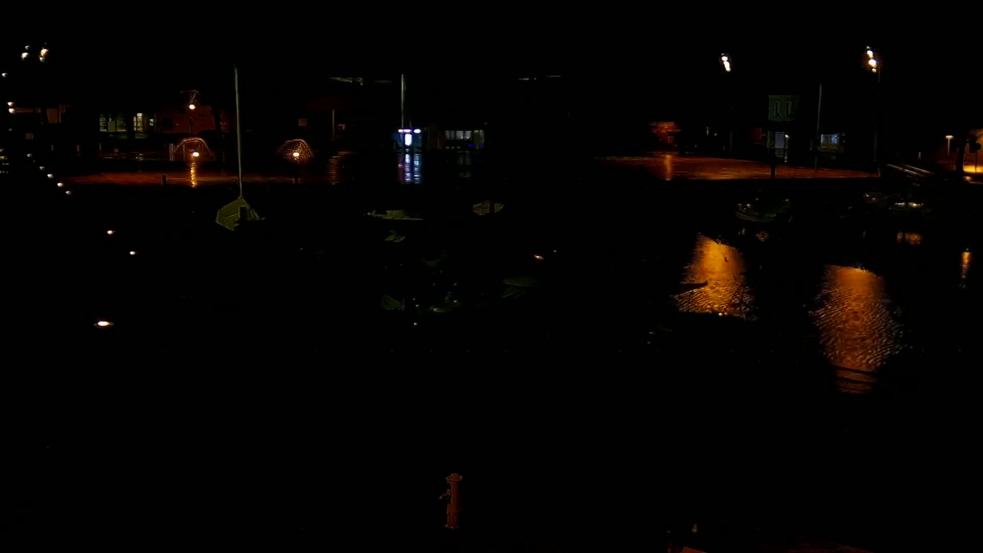 A nighttime view of a flooded area with several buildings and streetlights reflecting in the water.
