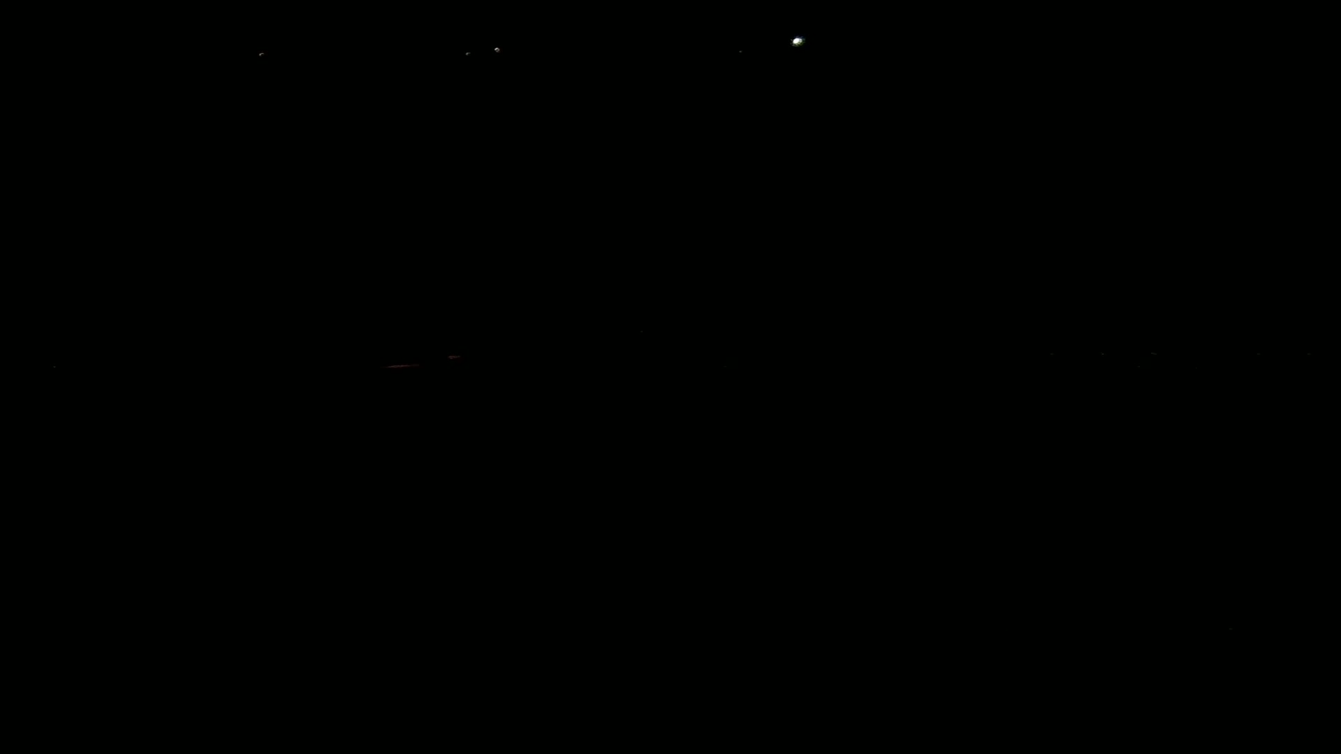 A dark, nighttime scene shows a faint horizon line with a few distant lights.