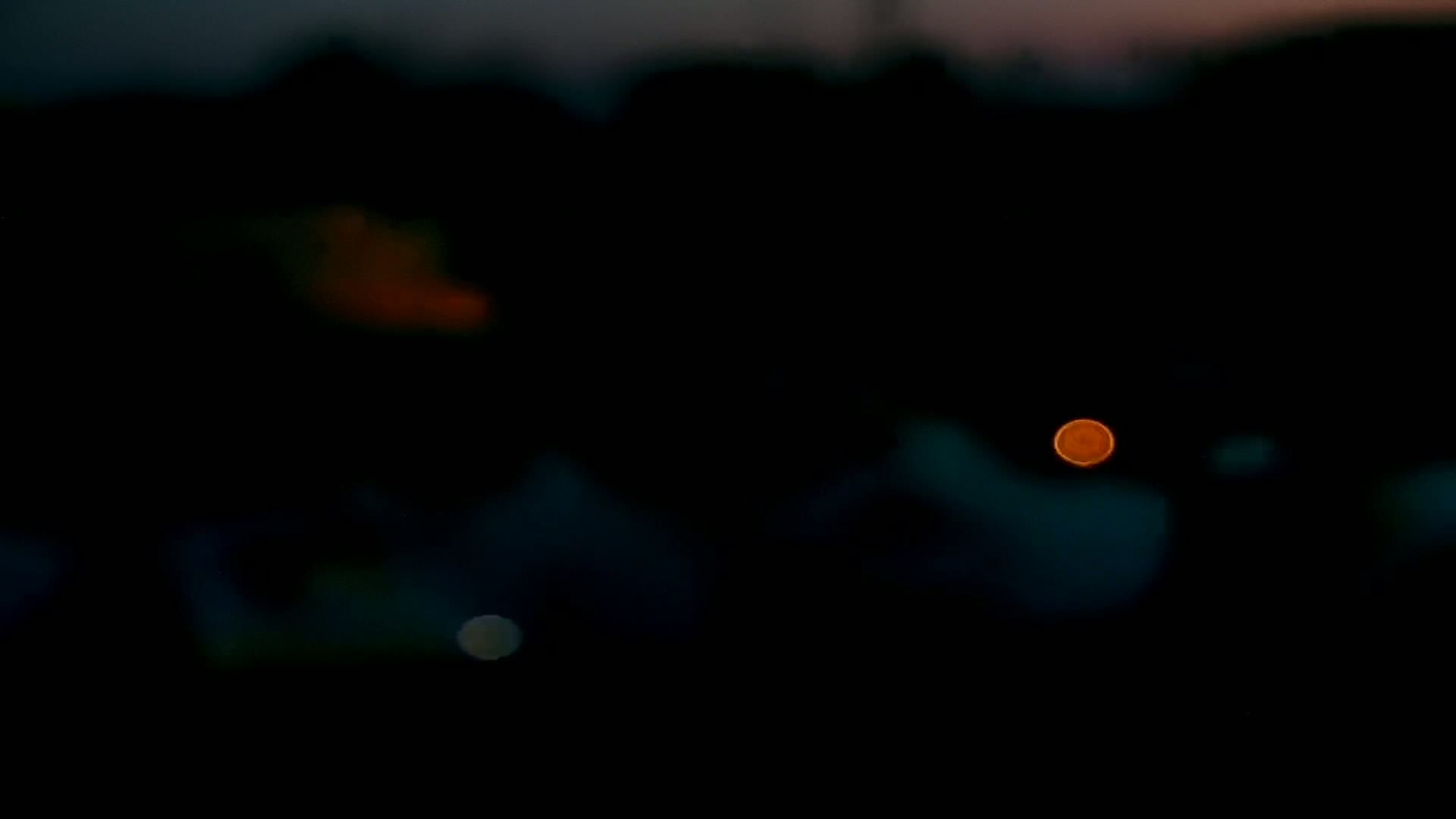 A blurred nighttime image shows a single, bright orange light and other indistinct lights against a dark background.