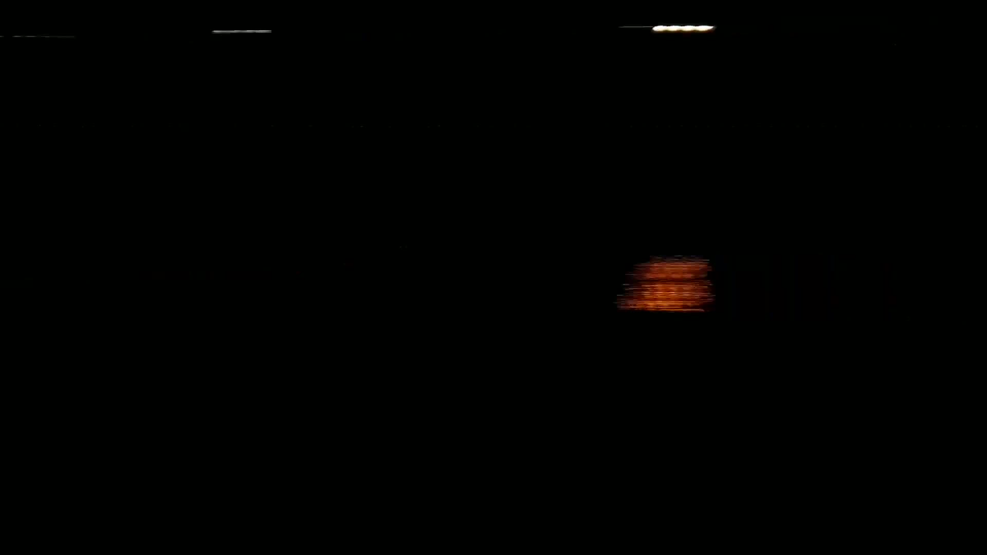 A blurry, orange light reflects on a dark body of water at night.