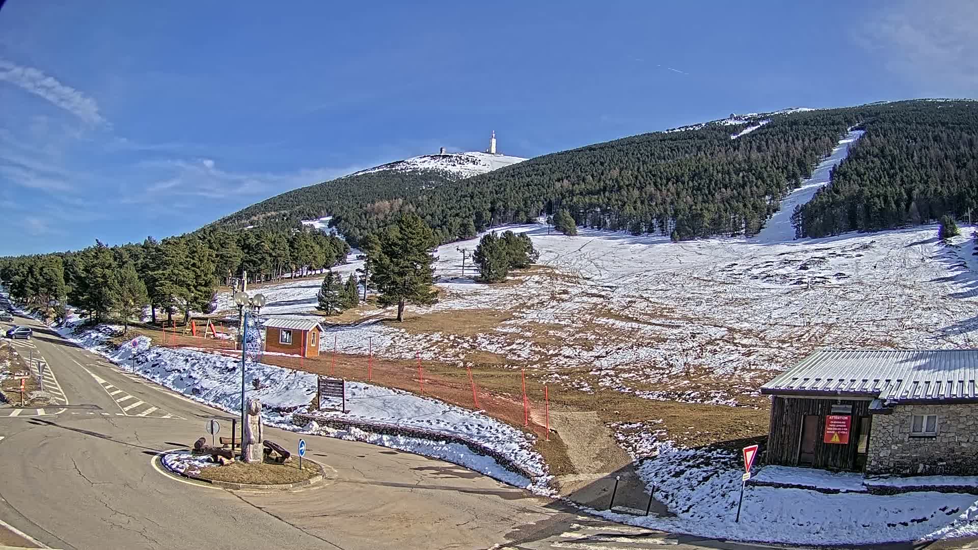 A mountain ski resort with a partially snow-covered landscape under a clear blue sky.