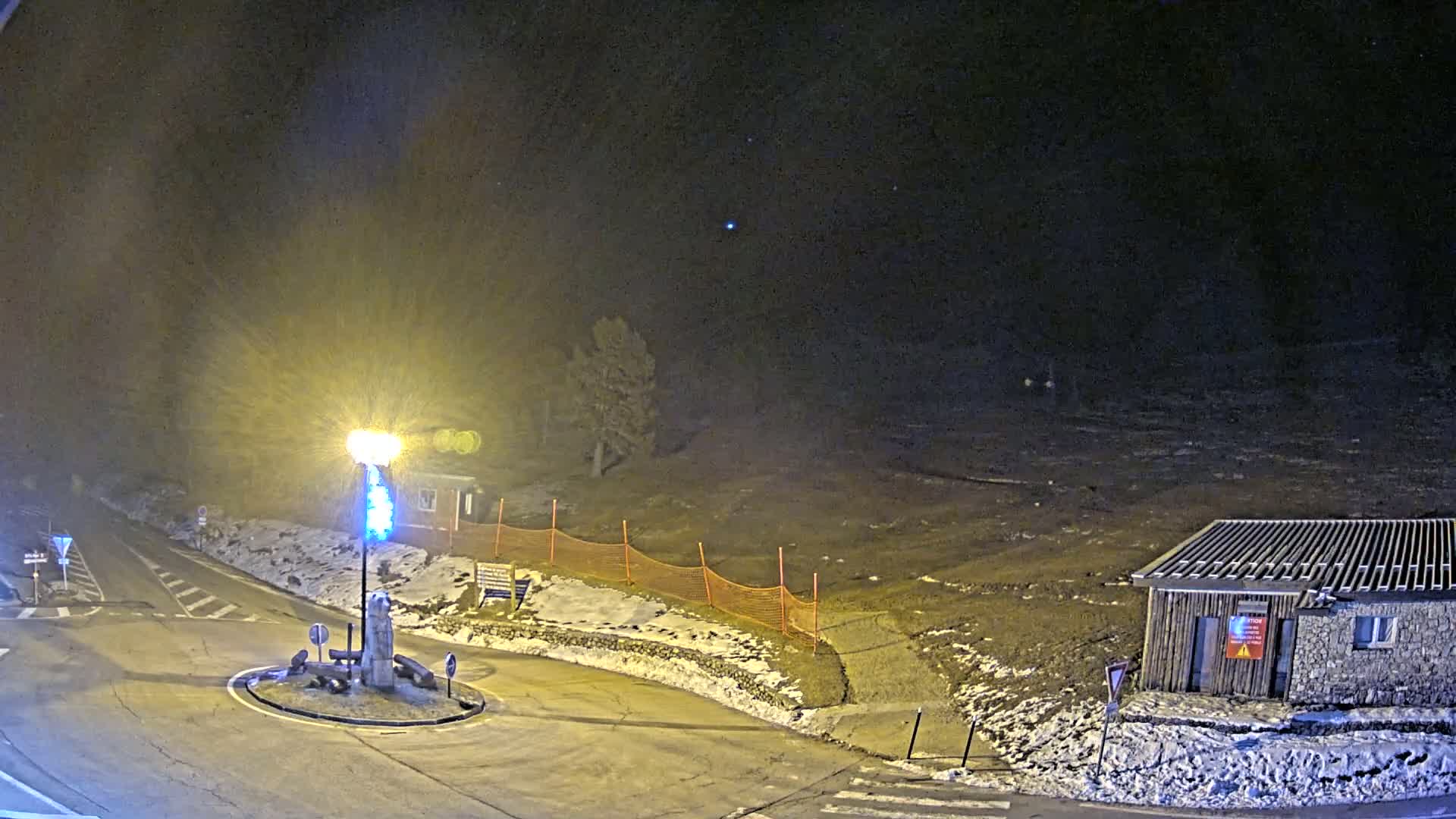 A nighttime view of a snow-dusted roundabout and small building under a dark, possibly snowy sky.