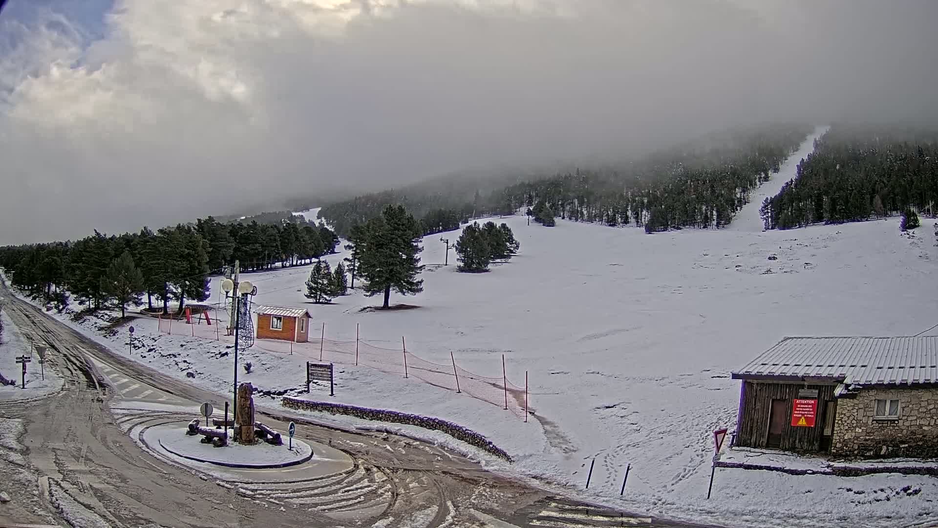 A snow-covered ski slope with a few buildings and a road is visible under an overcast sky.