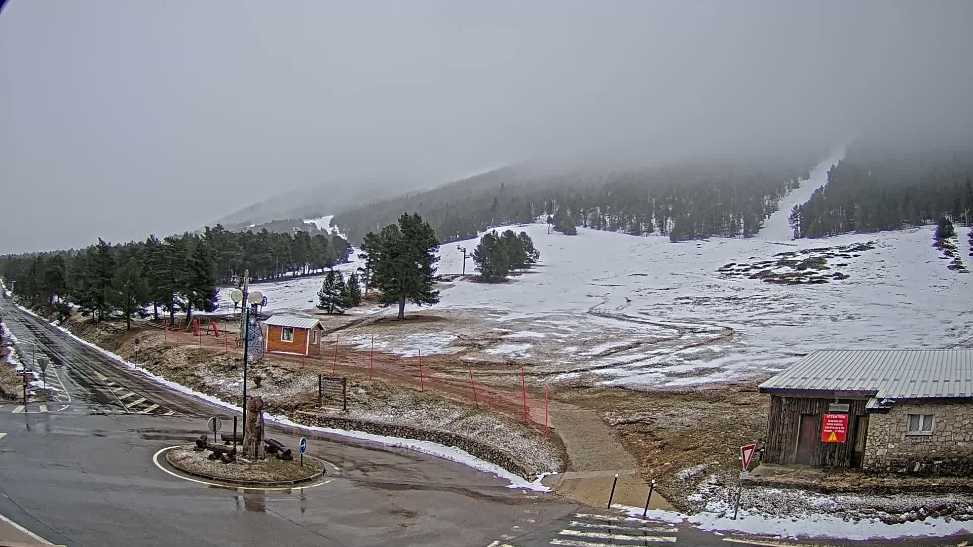 A wet, overcast day at a snow-covered ski resort with a few small buildings and a road leading into a roundabout.