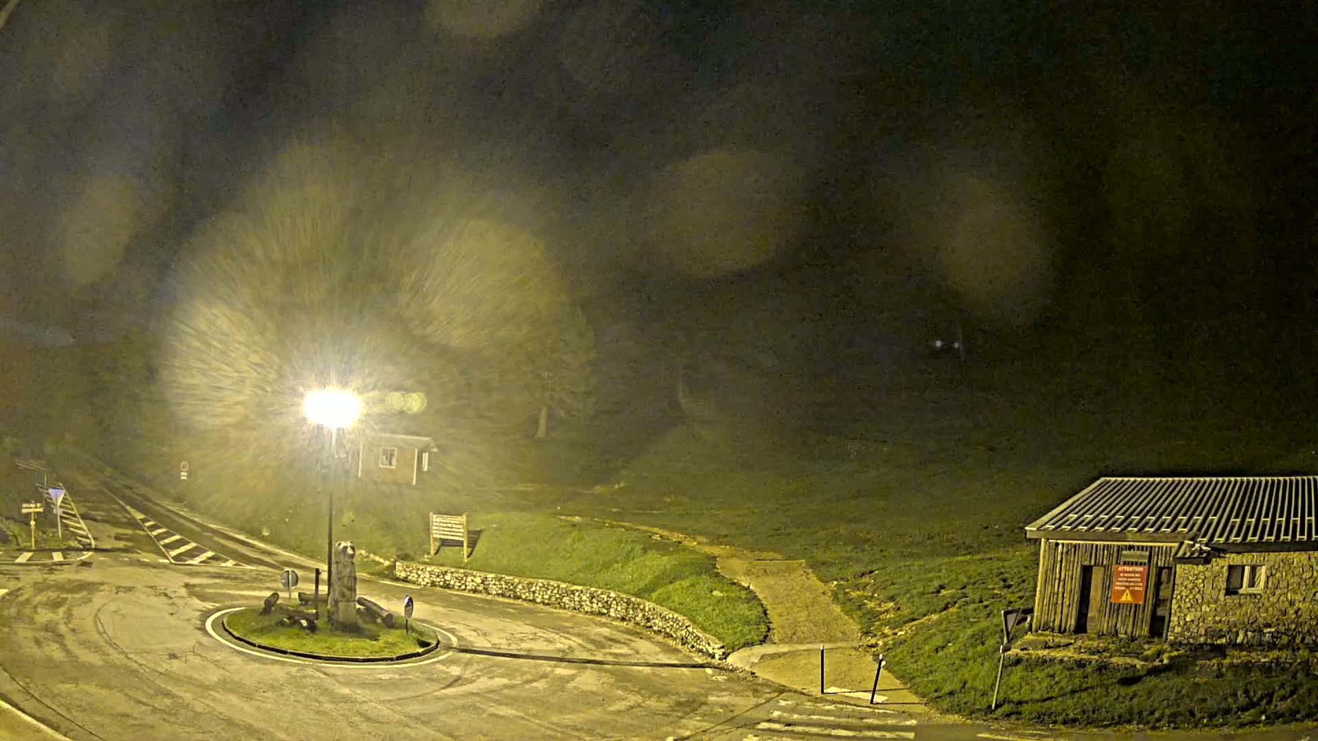 A nighttime scene of a roundabout and small building in a misty, dimly lit area.