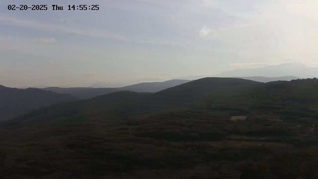 A hazy, somewhat overcast day reveals a panoramic view of rolling, dark green hills and mountains extending to the horizon.