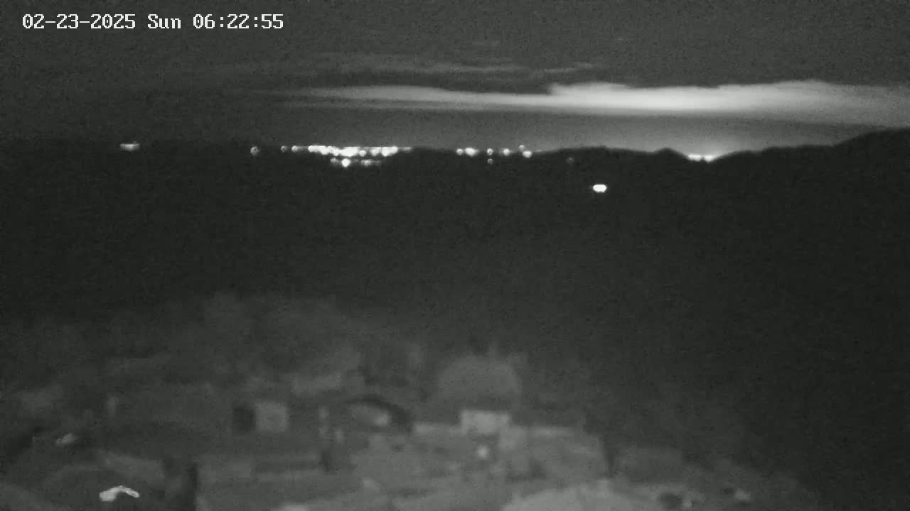 A nighttime, low-light view shows a distant city skyline illuminated, with a dark, possibly mountainous, foreground and a mostly clear sky.