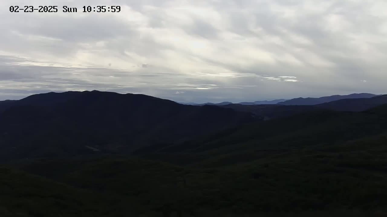 A view of dark, rolling hills under a mostly cloudy sky.