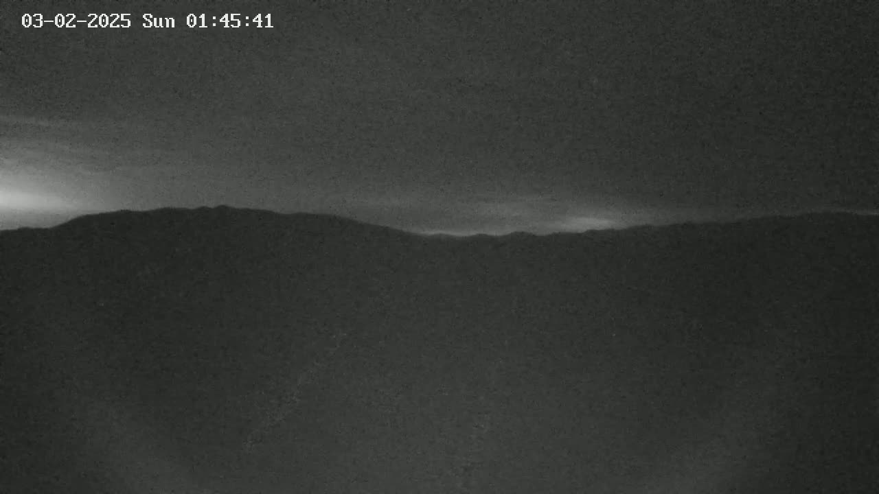 A dark, nighttime image shows a low-lying mountain range under a mostly clear sky.