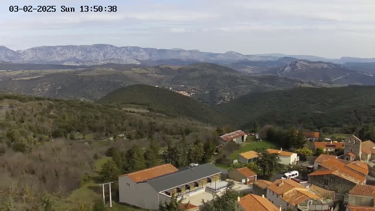 A small village with red-tiled roofs nestled in a mountainous region under a partly cloudy sky.