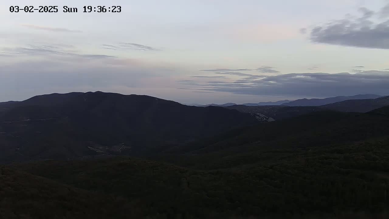A view of dark, rolling hills and mountains under a cloudy, twilight sky.