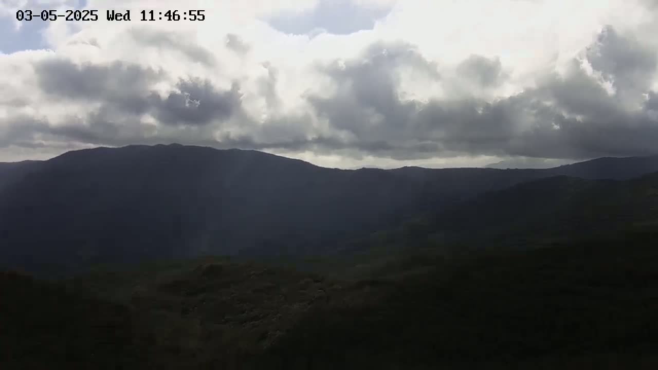 A mostly cloudy sky hangs over dark, distant mountains and a shadowy foreground.