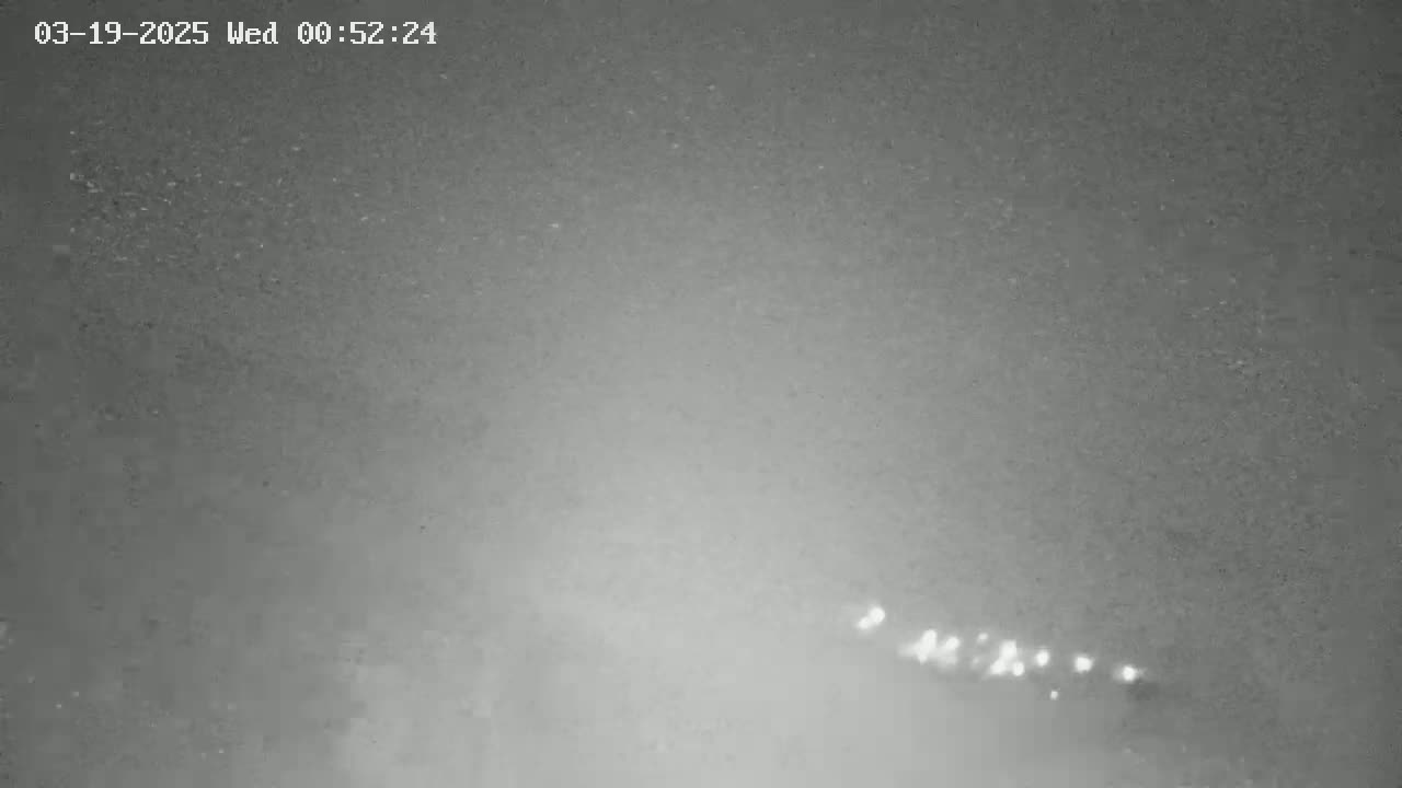 A nighttime, low-light image shows a blurry view of a road with distant headlights visible in the lower center.