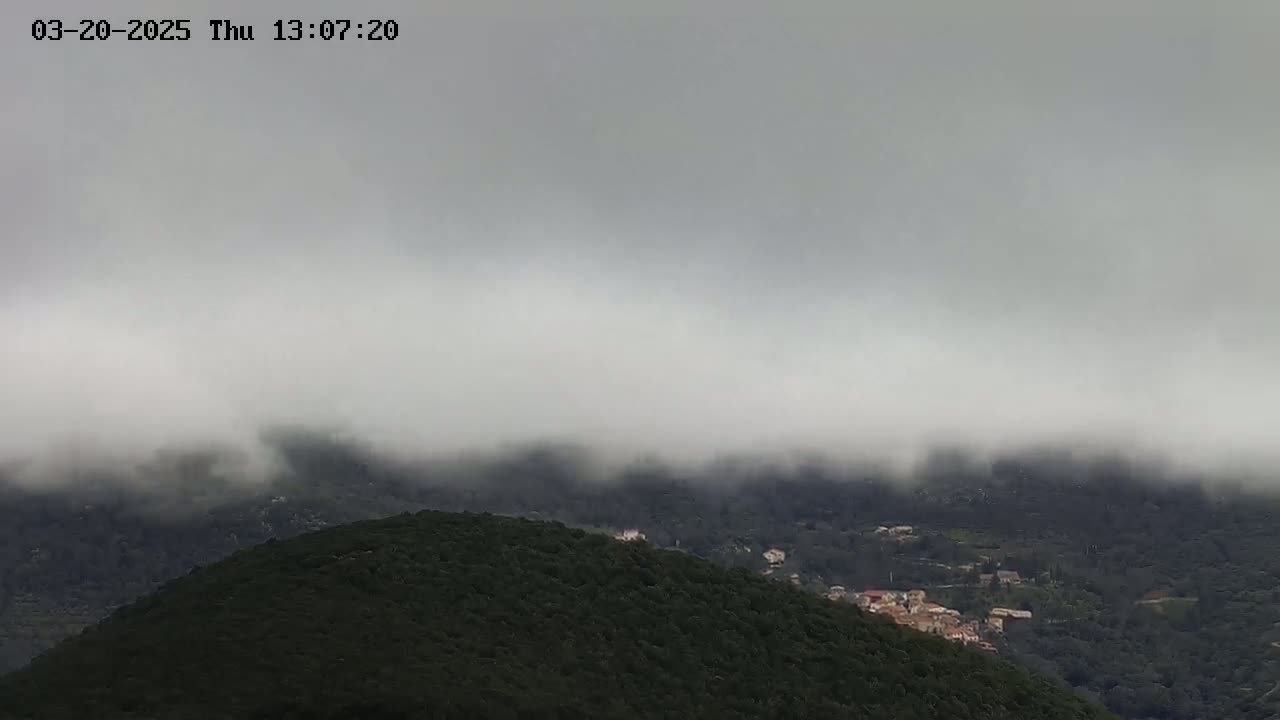 A low-lying fog obscures a hilly landscape with dark green vegetation and a small village nestled among the trees.
