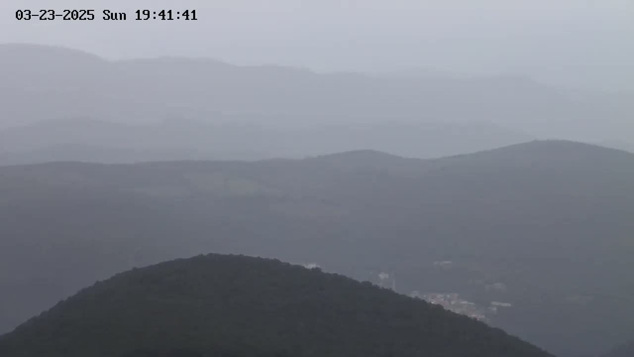 A hazy, overcast day reveals a series of rolling, dark green hills and mountains in the distance.