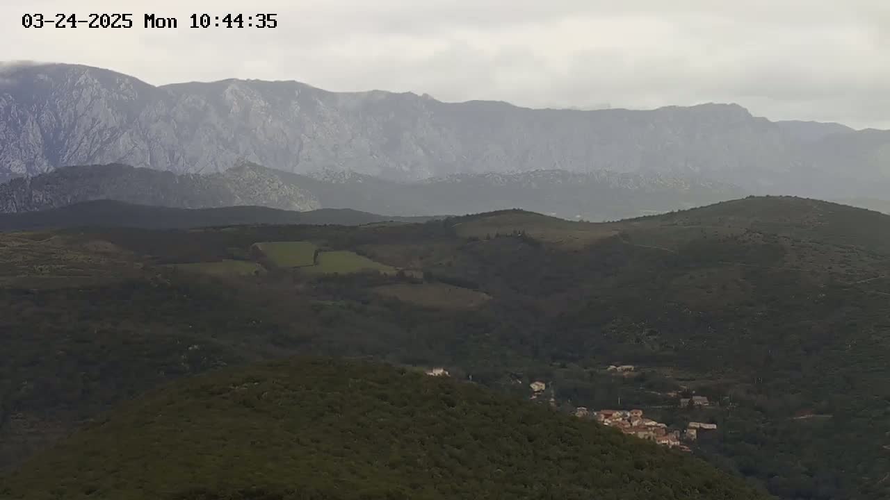 A hazy view of rolling hills and mountains under an overcast sky, with a small village nestled in the lower hills.