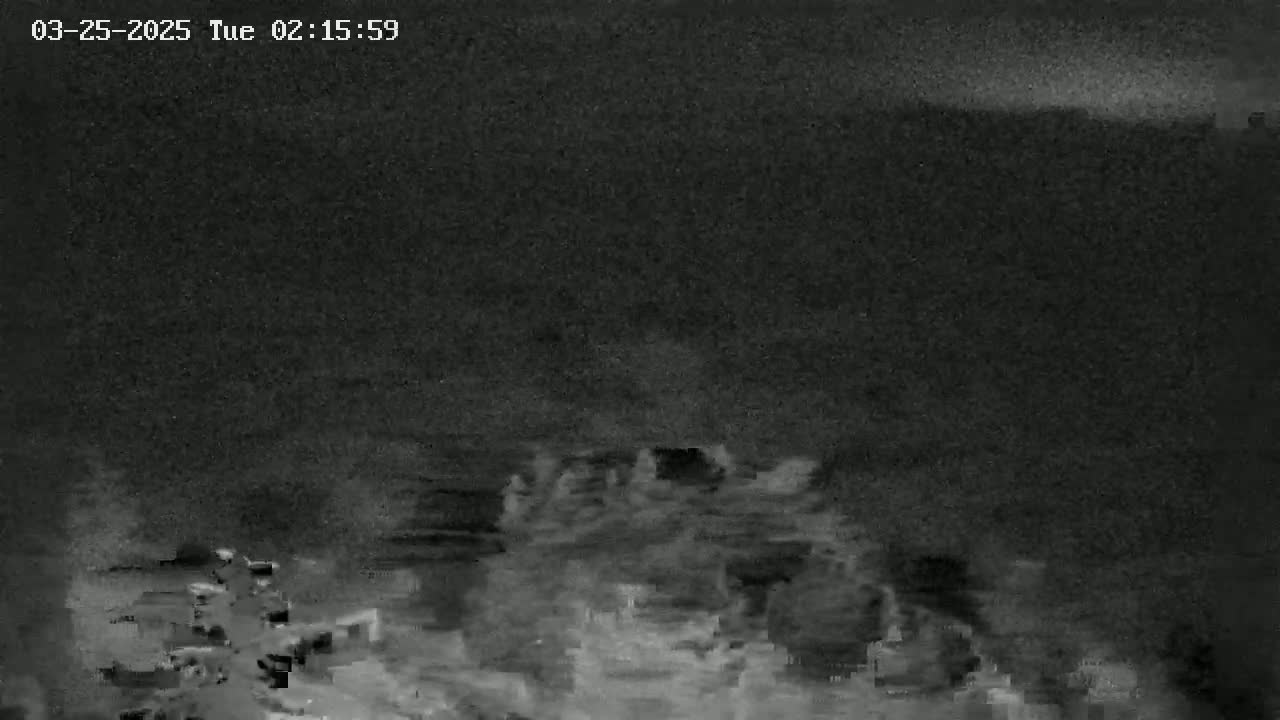 A low-light, grainy image shows a dark, possibly nighttime scene of what appears to be a body of water with indistinct shapes possibly representing boats or structures on the water.