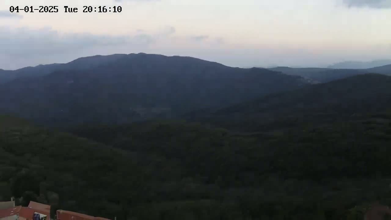 A twilight view shows a series of dark green hills and mountains under a pale, cloudy sky.