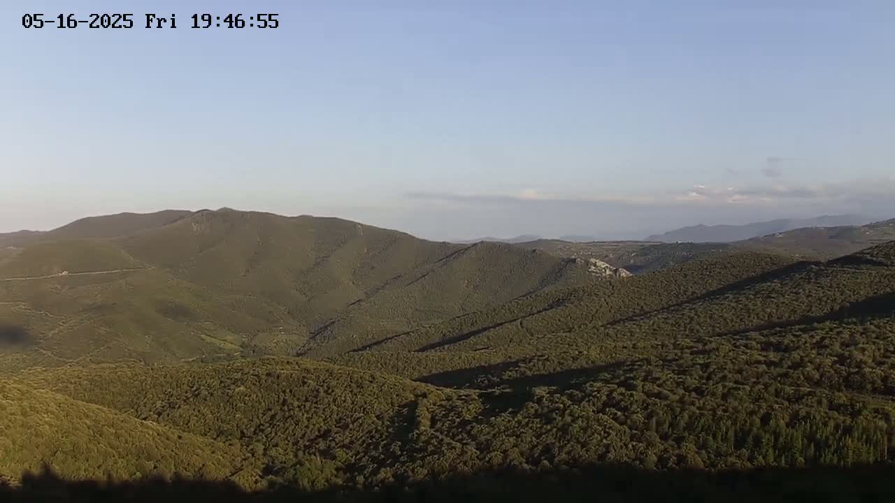 A vast expanse of rolling, forested hills stretches to the horizon under a clear, light-blue sky.