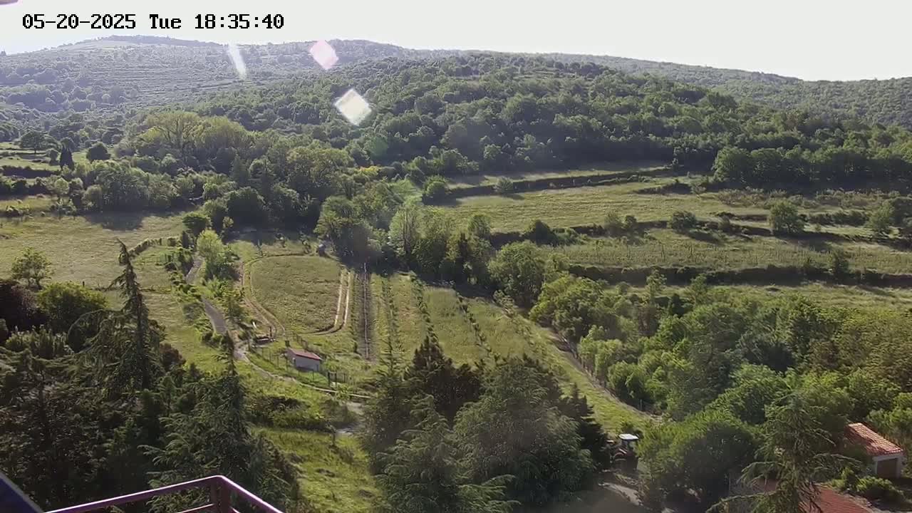 A sunny, high-angle view of a rural landscape with rolling green hills, fields, and trees.