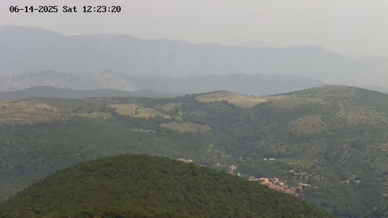 A hazy view of rolling green hills and mountains, with a small village nestled in the valley below.