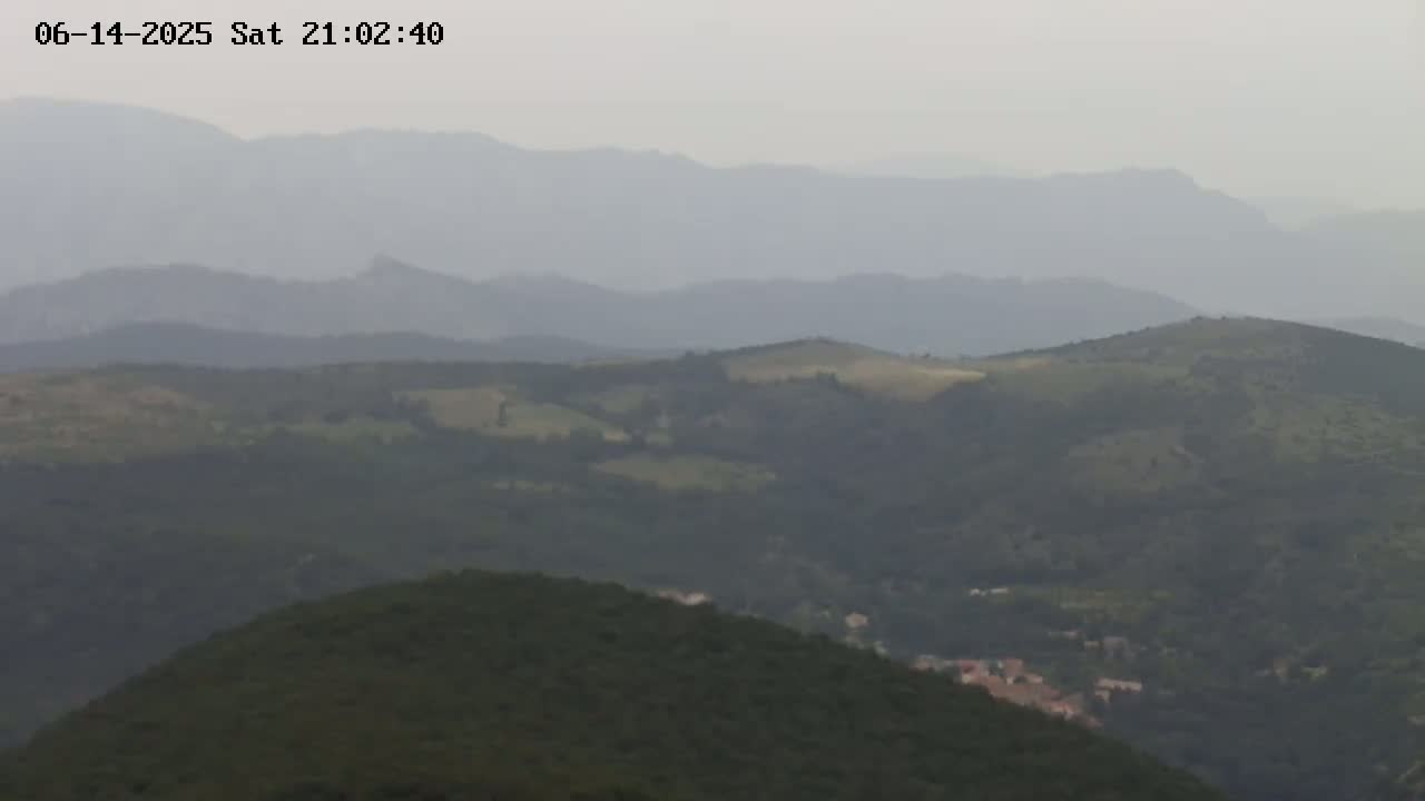 A hazy view of rolling hills and distant mountains, with a small village nestled among the greenery.