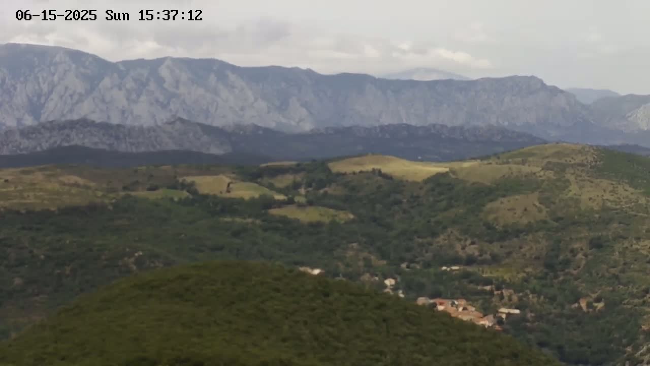 A hilly landscape under a cloudy sky shows rolling green hills and mountains in the distance.