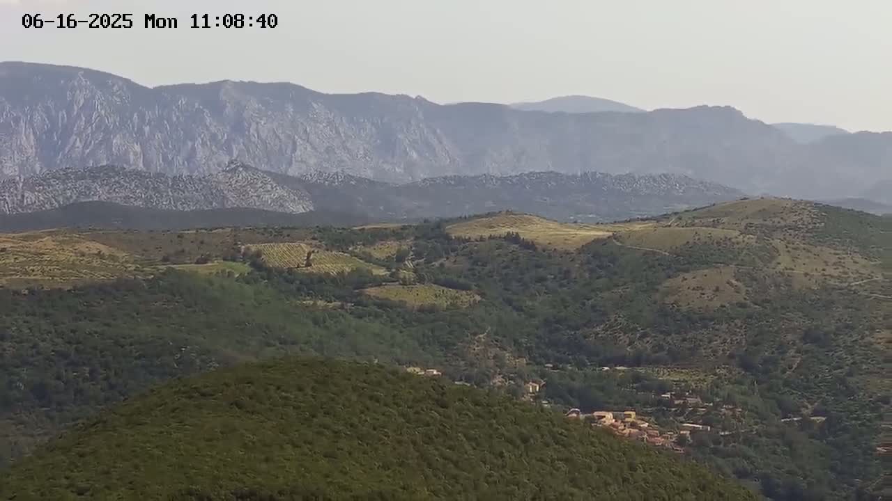 A hazy view shows rolling hills and mountains covered in green vegetation, with a small village nestled in the valley below.