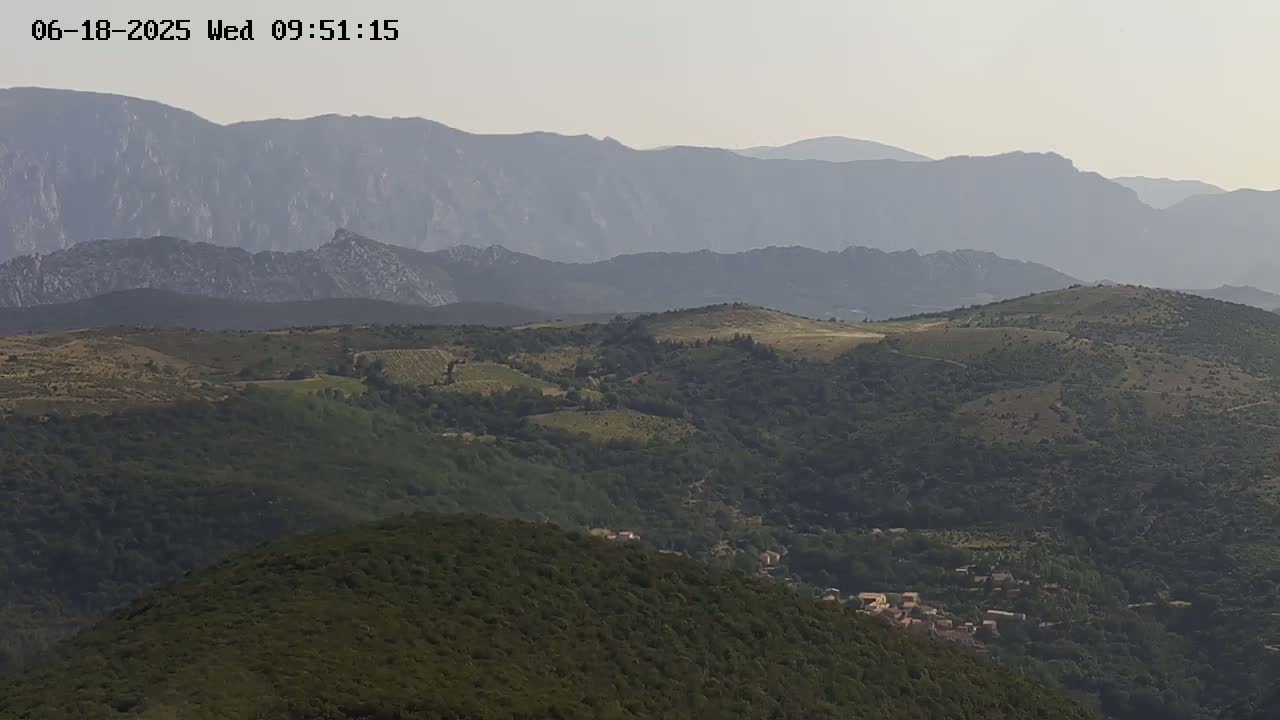 A hazy view shows rolling green hills and distant mountains under a light, overcast sky.