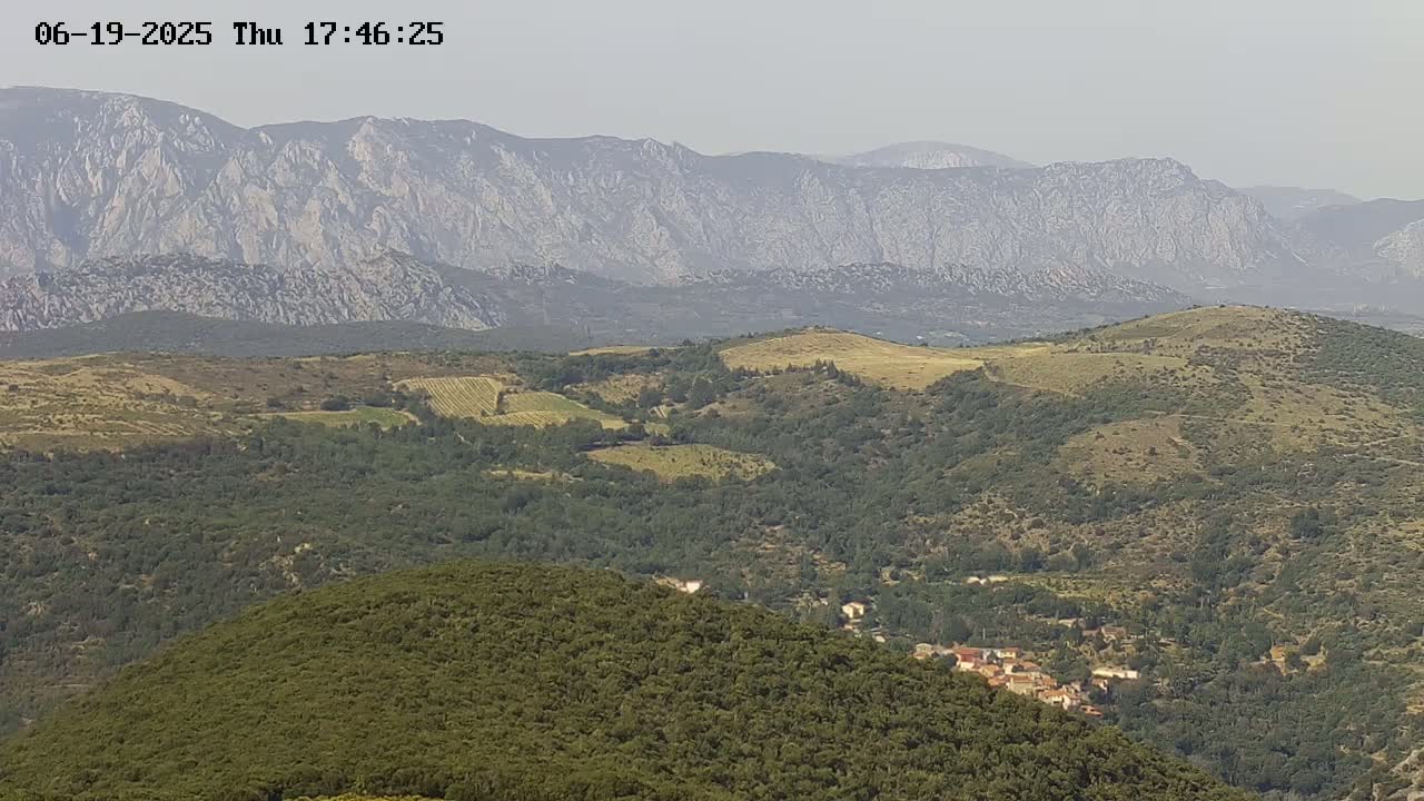 A hazy, mountainous landscape with rolling hills covered in green vegetation and a small village nestled among the trees in the foreground.