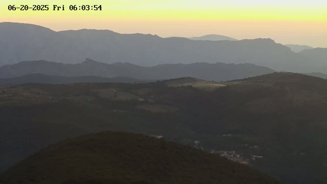 A hazy sunset illuminates rolling hills and distant mountains.