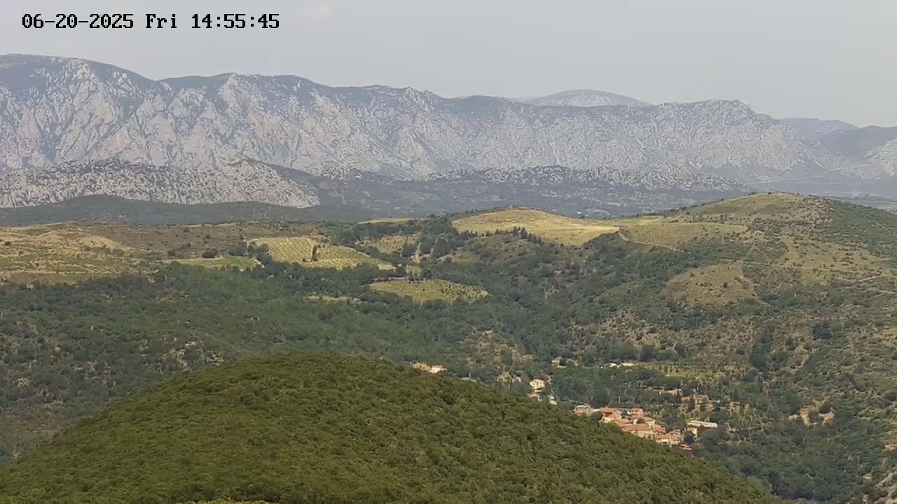 A hazy, mountainous landscape with lush green hills and valleys, featuring a small village nestled among the trees.
