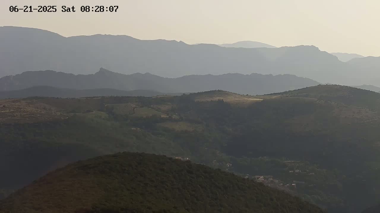 Rolling hills and distant mountains are visible under a hazy sky.