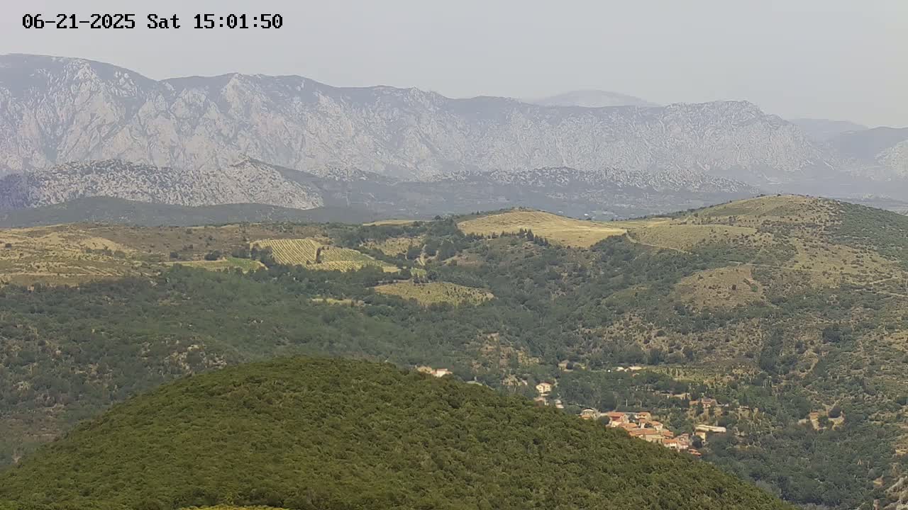 A hazy, mountainous landscape dotted with patches of green vegetation and a small village nestled in the valley below.