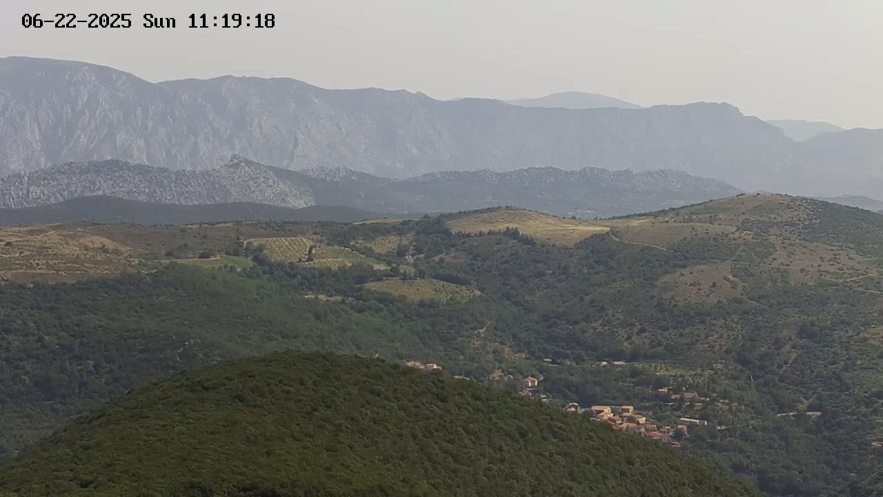 A hazy view of rolling hills and mountains, dotted with small villages and patches of vegetation.