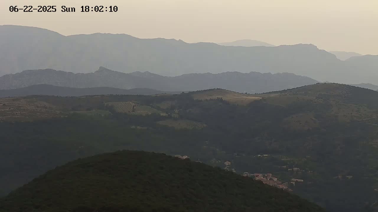 A hazy, mountainous landscape is visible, with layers of hills and valleys receding into the distance under a muted sky.