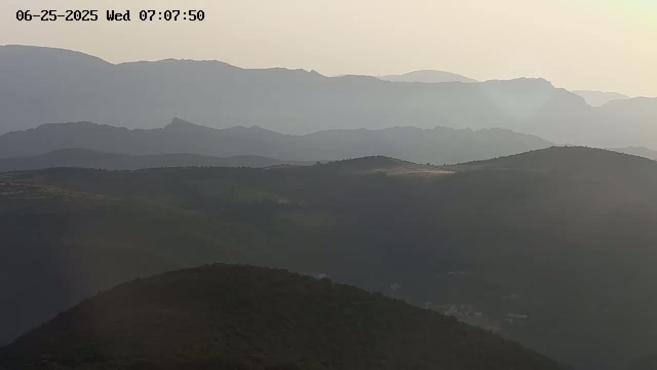 A hazy, light-colored sky overlooks a range of dark, rolling hills and mountains extending into the distance.