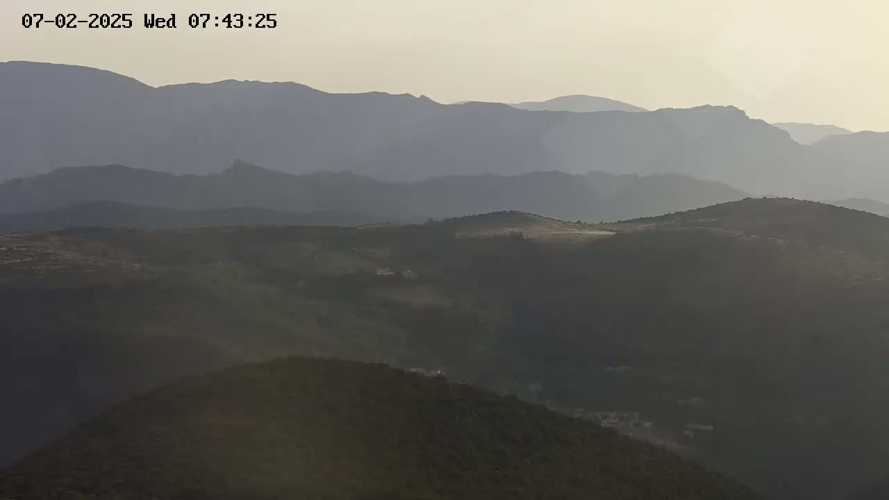 A hazy, sunlit view of rolling hills and distant mountains under a pale sky.