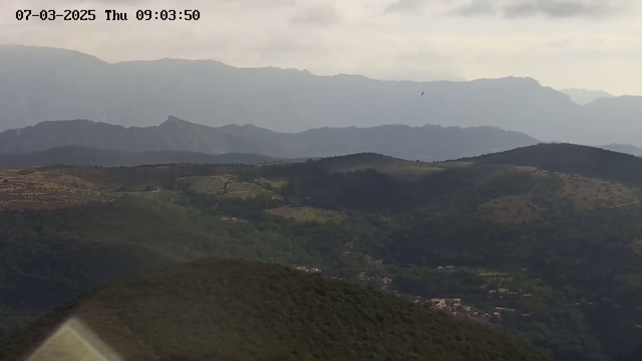 A hazy view of rolling hills and distant mountains under a cloudy sky.