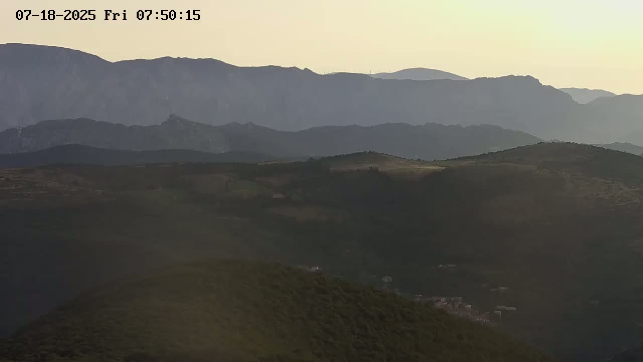 A hazy sunrise illuminates rolling hills and distant mountains.