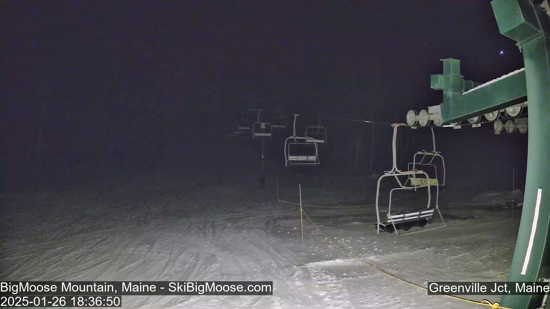 Under a dark night sky, several empty chairlifts are visible on a snow-covered ski slope.