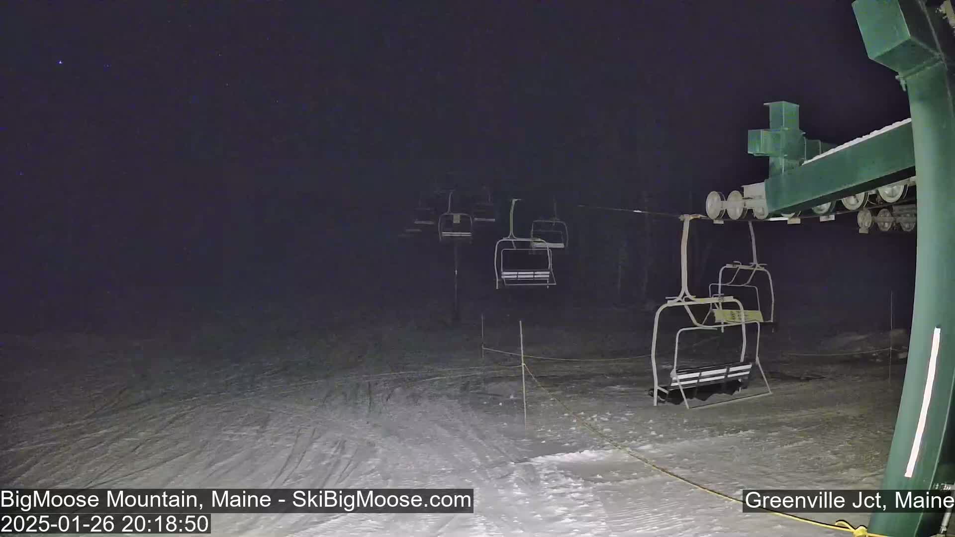 Under a dark, clear night sky, a snow-covered ski lift stands still with several empty chairlifts hanging from the cable.
