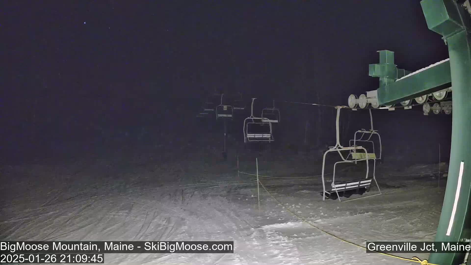 At night, under a clear, dark sky, several empty chairlifts are visible on a snow-covered ski slope.